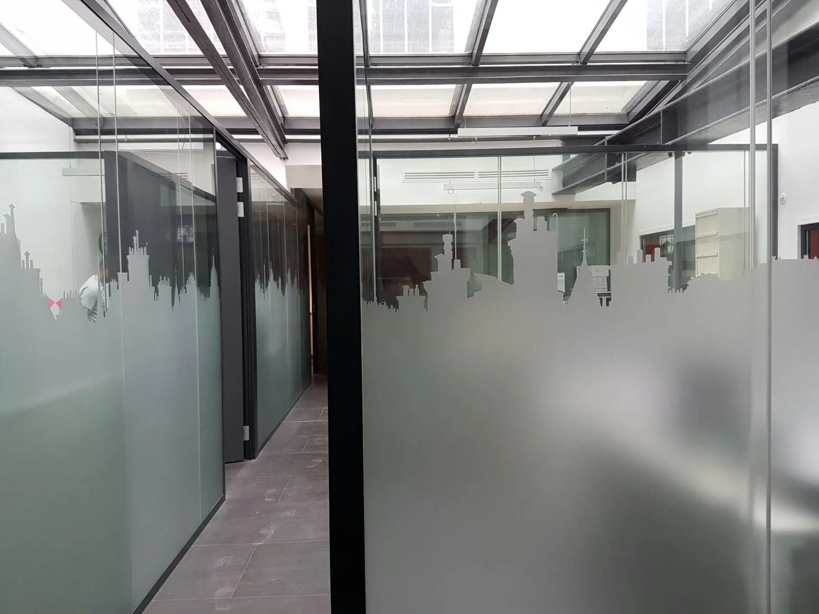 Couloir de bureaux dont les cloisons vitrées portent une skyline en film dépoli posée sur toute la longueur